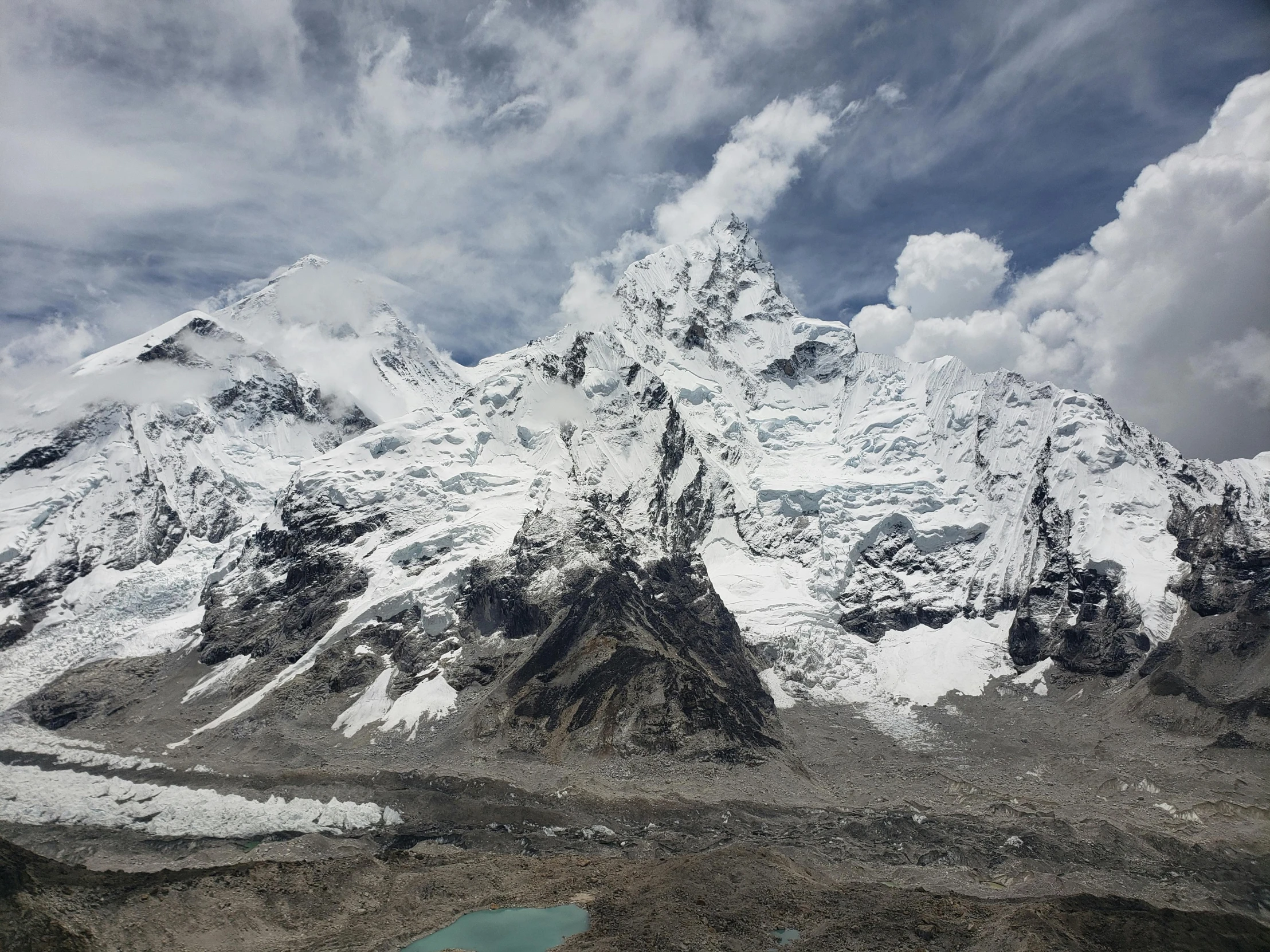 a snow covered mountain range under clouds and blue water