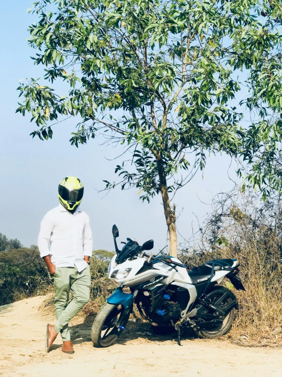 the man standing next to his motorcycle is looking at a tree
