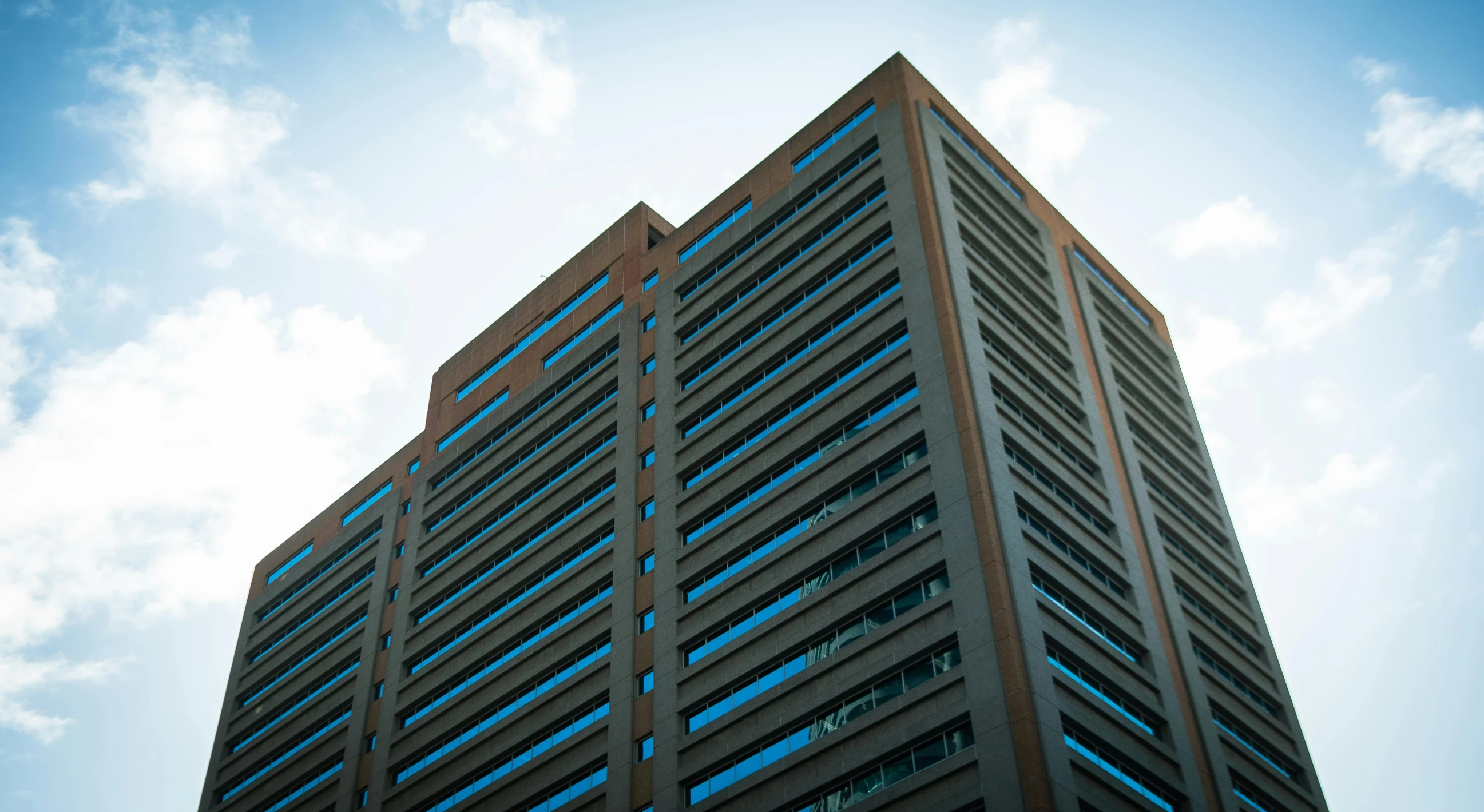 an office building with blue windows in the middle of a cloudy sky