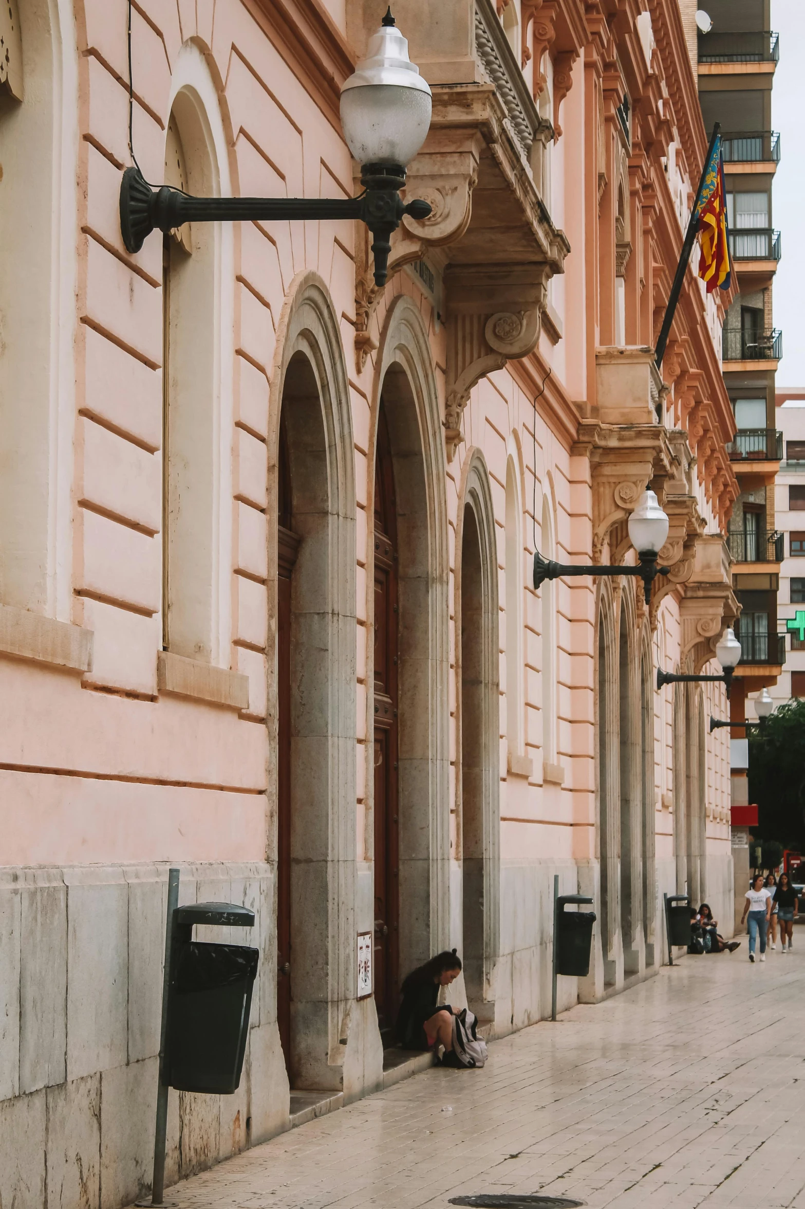 a person sitting on the sidewalk under an umbrella