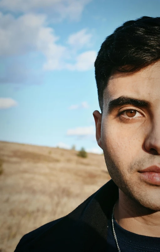 a man with a necklace on standing next to a field