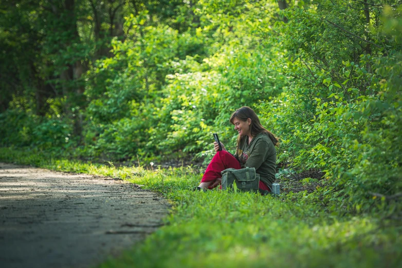 a woman sitting on the side of the road next to the woods