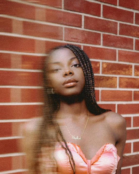 a woman in pink top and necklace standing against a brick wall