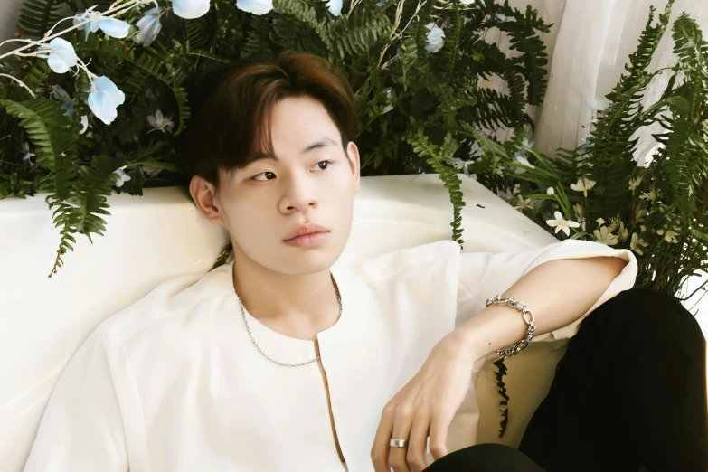 young asian male with black pants and white t - shirt seated next to flower decoration