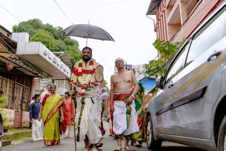 men with traditional garb walking in the street carrying umbrellas