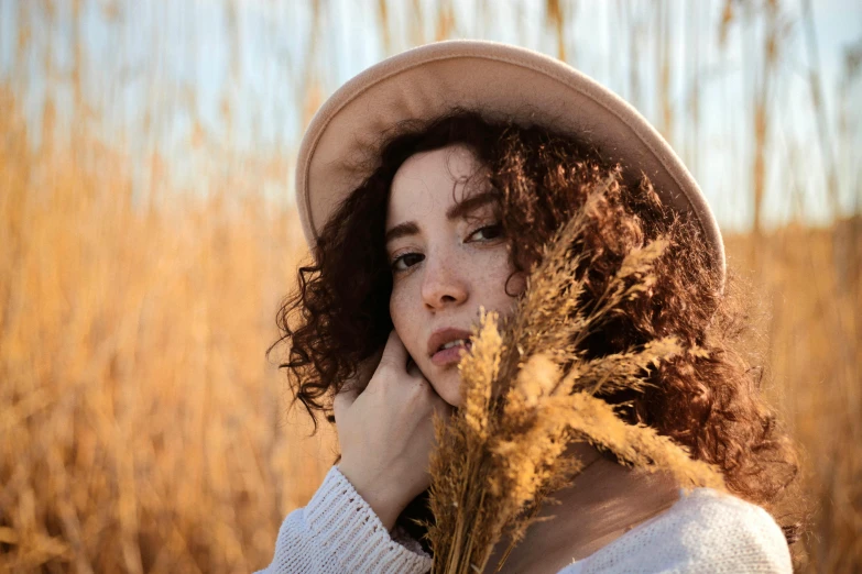 a woman in a hat standing in some dry grass