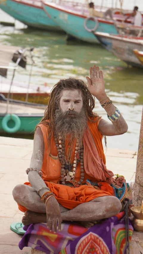 a male with long hair sitting down in a meditation pose