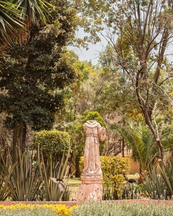 the statue is in a garden surrounded by trees and plants