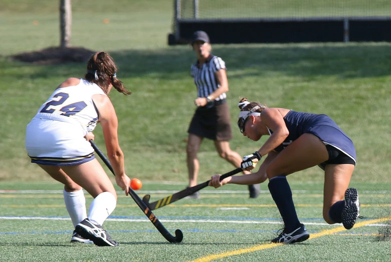 three female lacrosse players play with ball on field