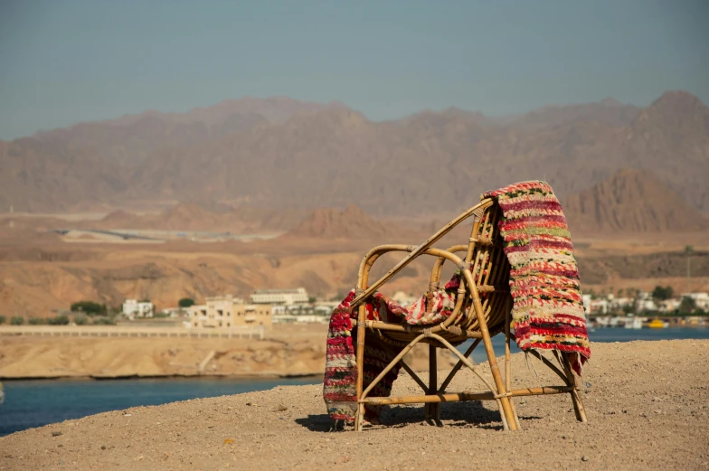 a chair sitting in the sand near water and mountains