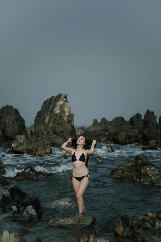 a person in a bikini standing in the water by rocks