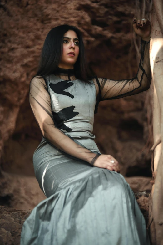 a young woman with long hair sitting on a rock formation, posing for a pograph