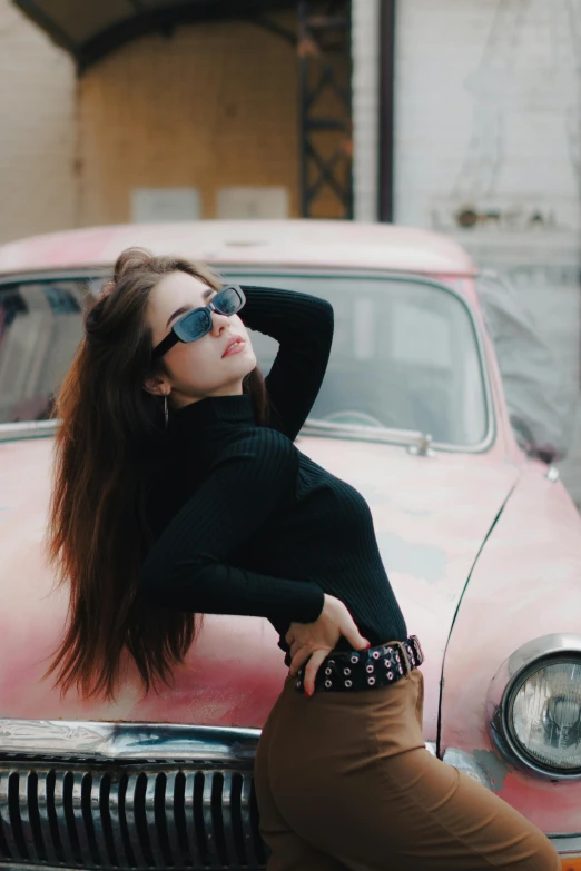 an attractive young woman leaning on the hood of a car