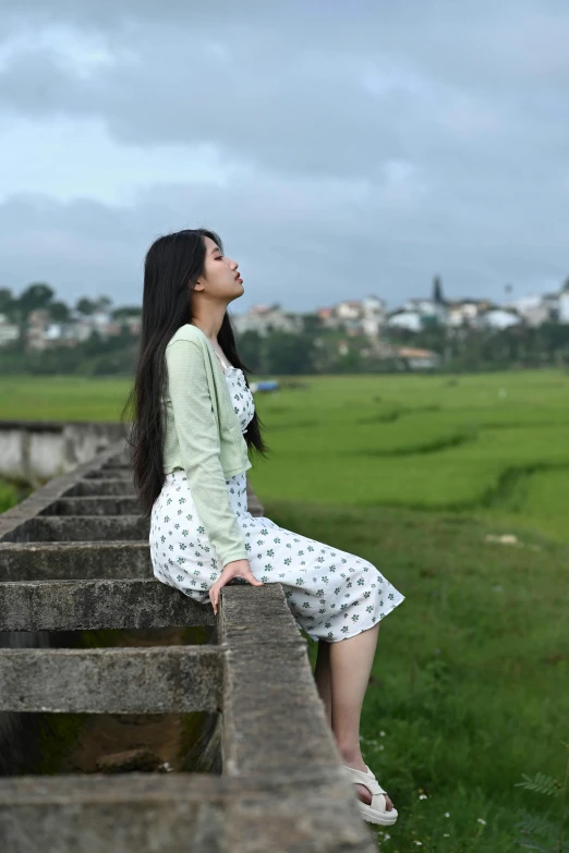 a girl sitting on concrete wall looking up into the sky