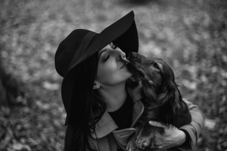 a black and white po of a girl wearing a hat kissing a dog