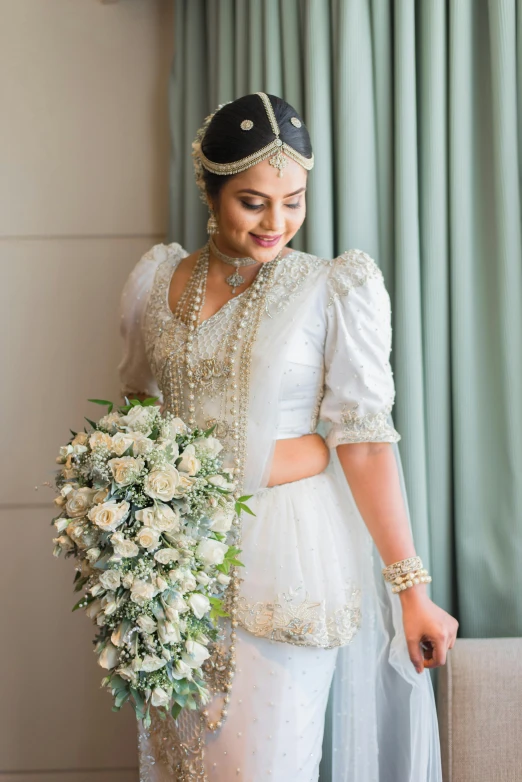 a woman in white is holding flowers while looking down at the floor