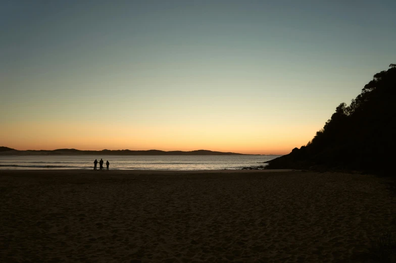 two people are walking down a beach at sunset