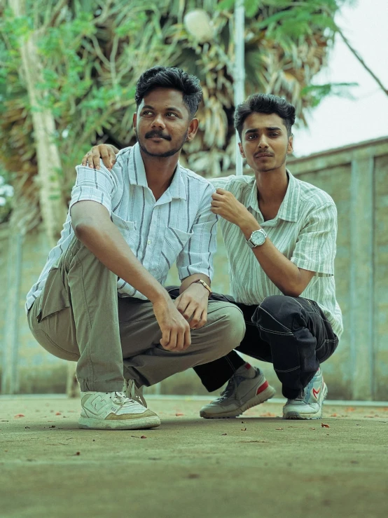 two men crouching next to each other in front of a fence