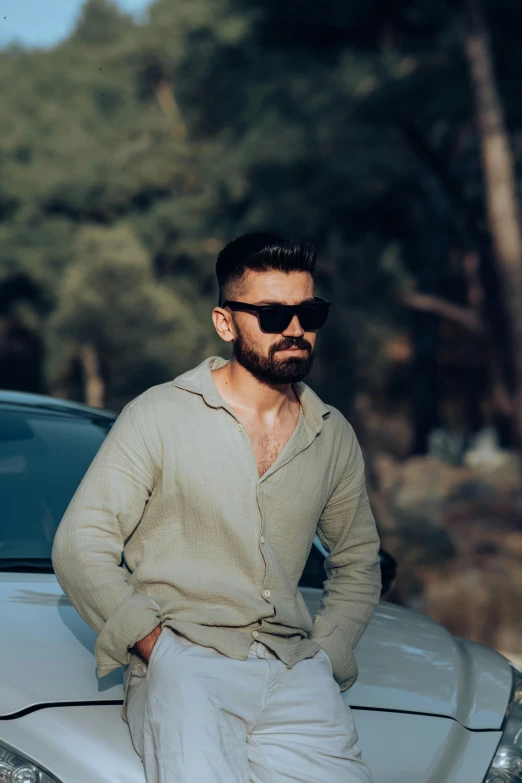 a man leaning against a white car wearing sunglasses