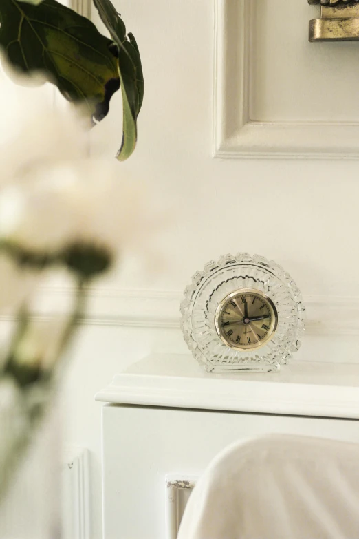 a clock on a dresser next to a vase of flowers