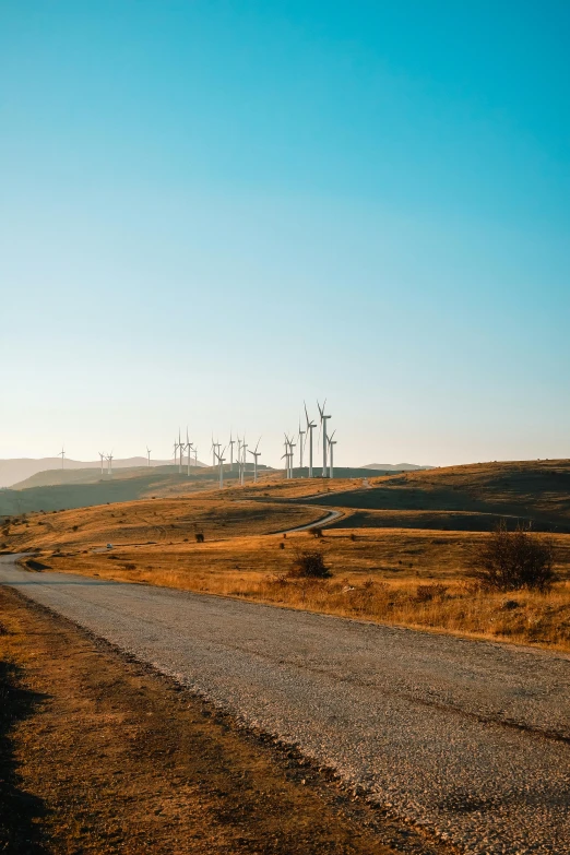 a dirt road on a hillside with many windmills in the background