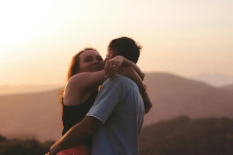 two people are hugging in the sunset with a view of mountains