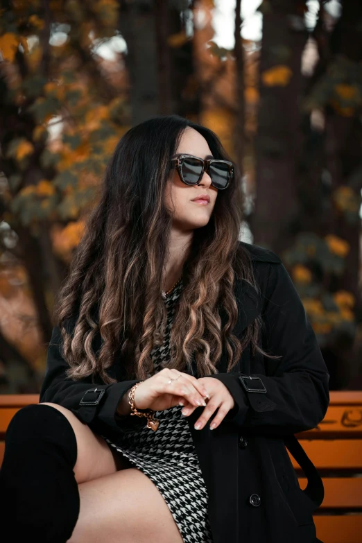 a woman with long, black hair and large sunglasses sits on a bench