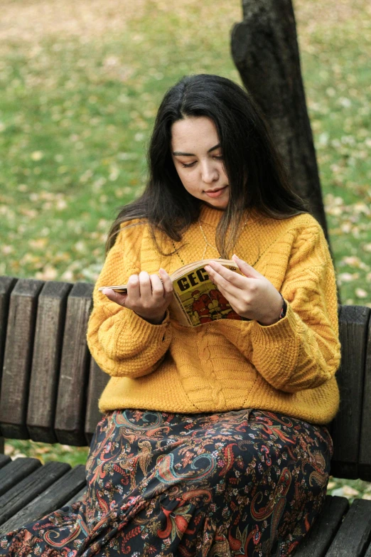 a woman sitting on a bench in front of a tree looking at a book