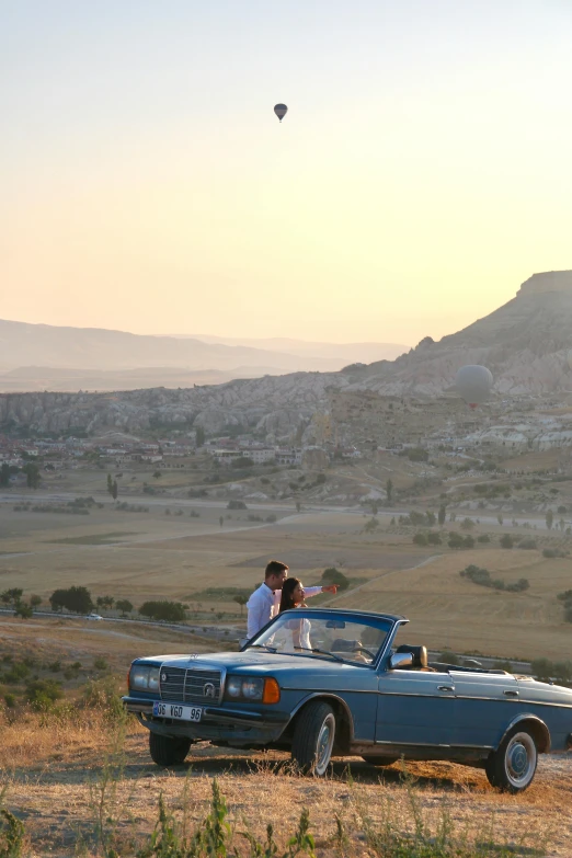 two people in the open convertible car near a  air balloon