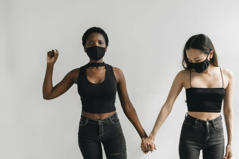 two women with facemasks and black s hold hands