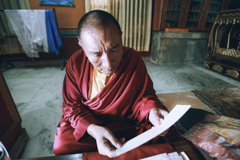 an older man in red sits and reads through a paper