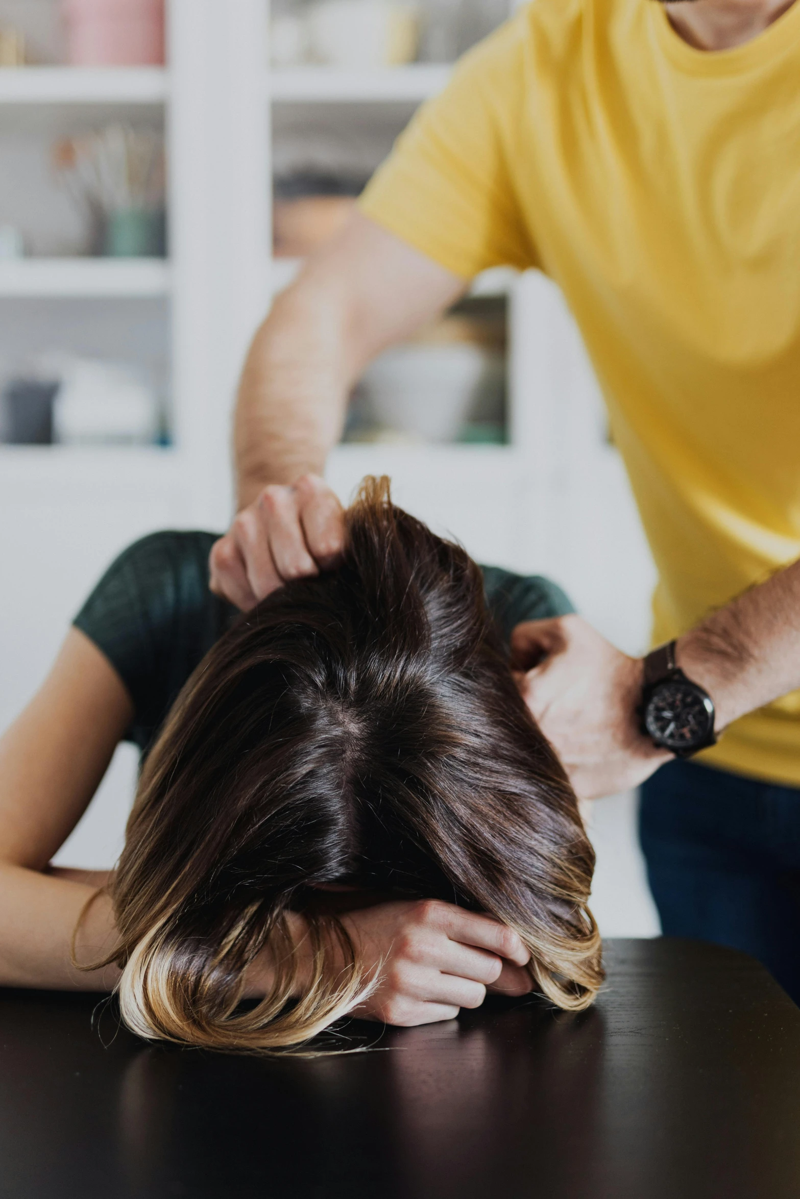 the man is sitting at the table and holding his head in front of the girl