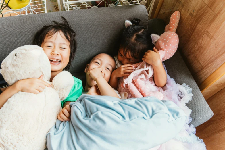 three little girls laying on a couch next to a stuffed animal