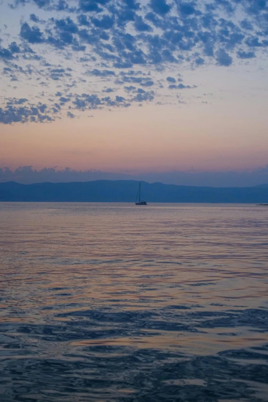 two sailboats anchored on the ocean at sunset