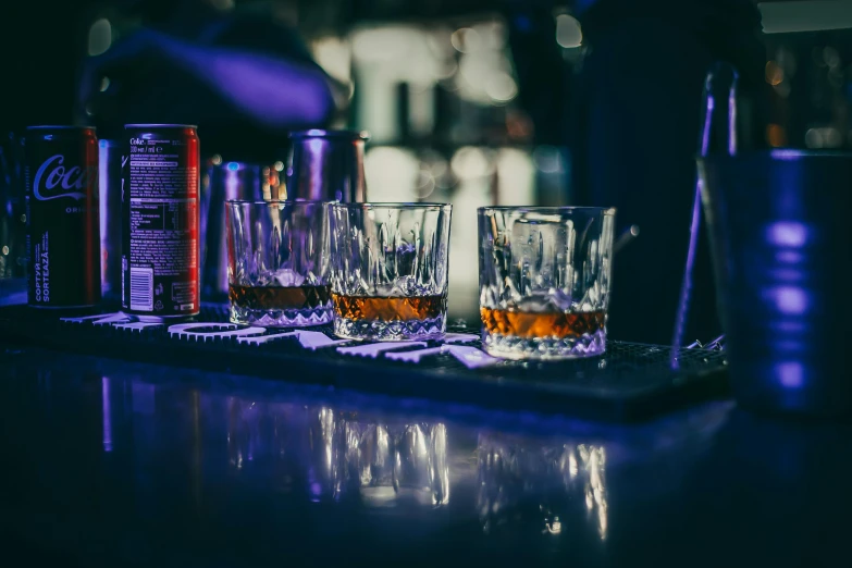 many bottles are sitting on a bar near three glasses