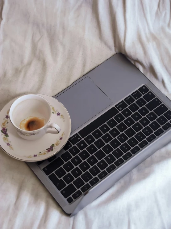 a laptop is on a bed with an espresso cup next to it