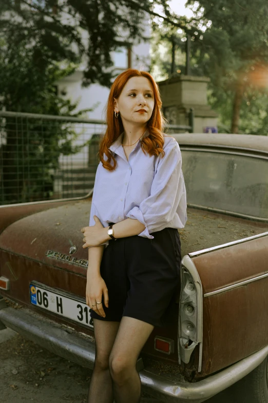 a young woman with red hair poses in front of a car