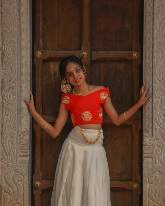 a  in an orange and white dress and matching skirt poses by a door with her arms stretched out