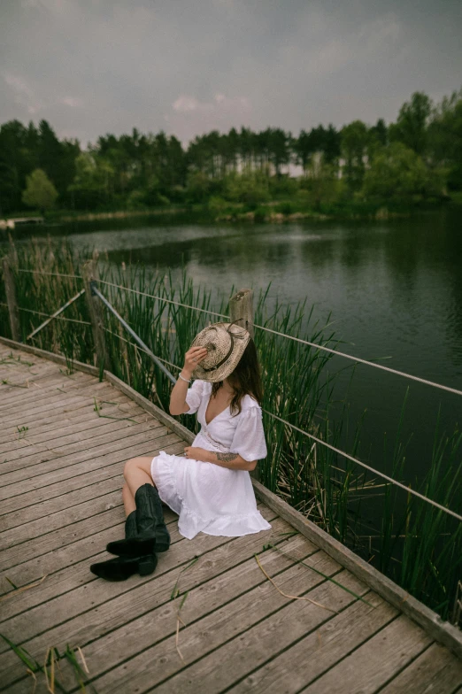 a woman wearing a white dress and a hat sits on a boardwalk