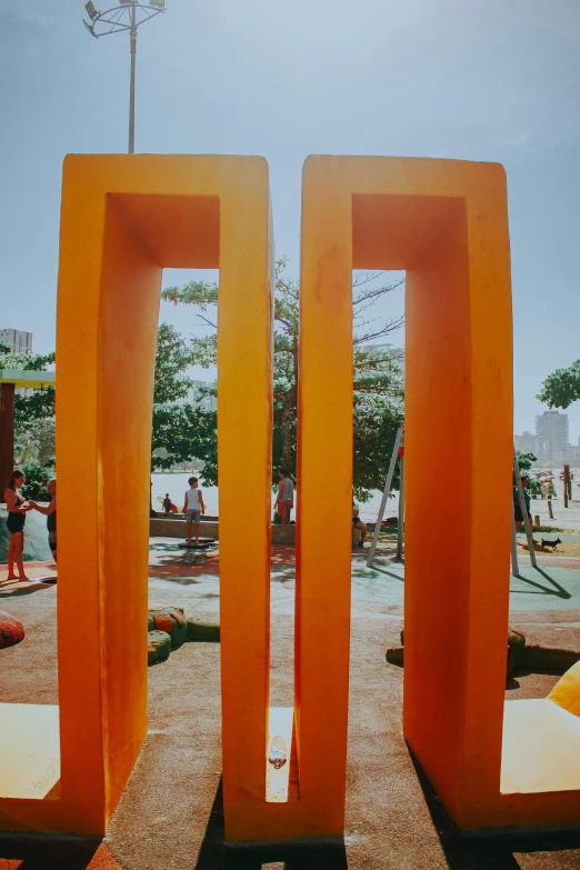 a sculpture of two orange columns in front of a park