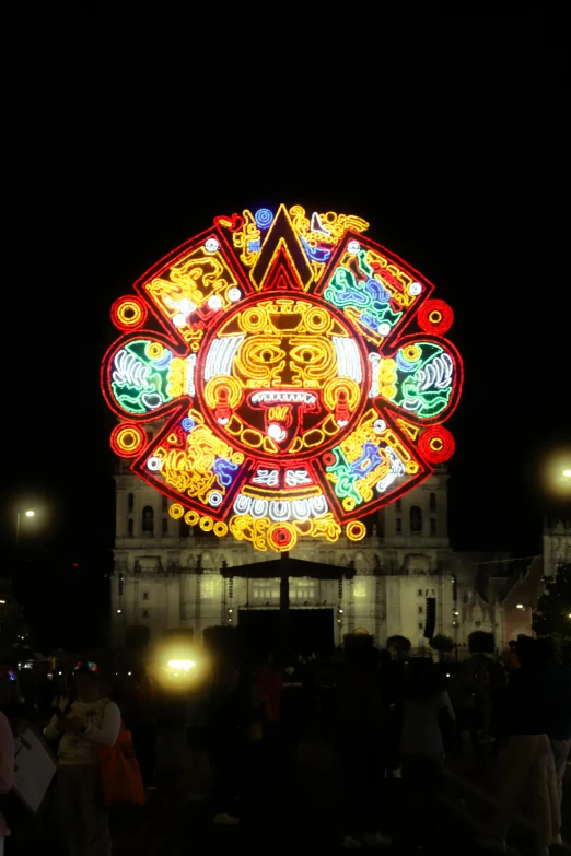 people looking at an illuminated clock in the middle of a nighttime scene