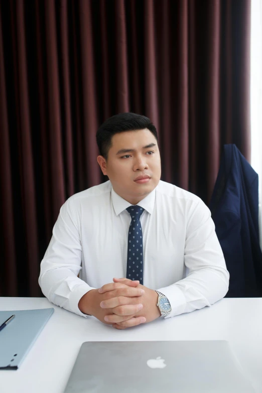 an asian businessman sits at his desk while staring at the camera