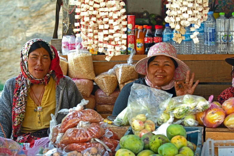 two women sitting in front of a fruit stand