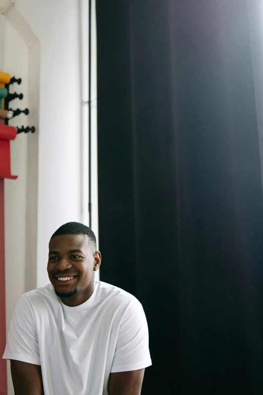 a man in a white t - shirt sits in front of a wall