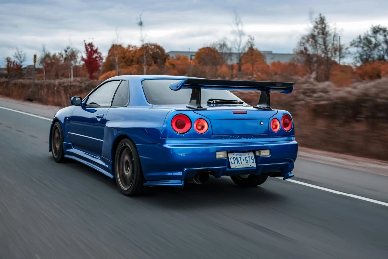 a blue car driving down a road in autumn