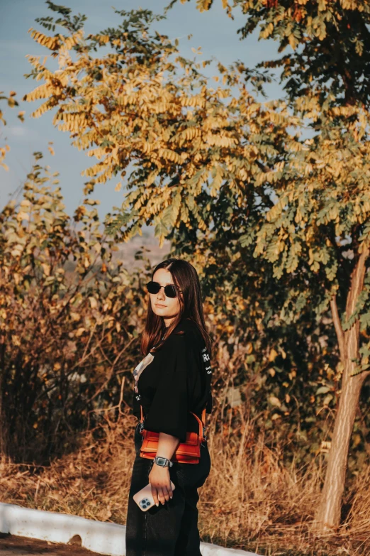 woman with sunglasses holding a skateboard near trees