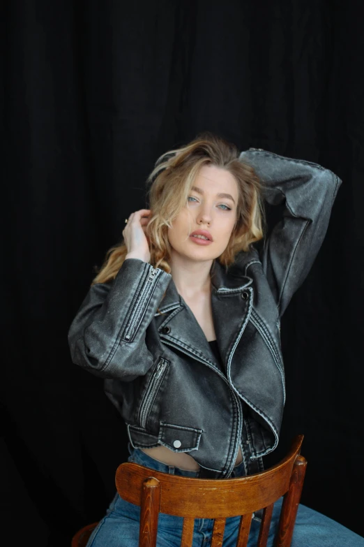 a girl in a black jacket leaning up against a chair