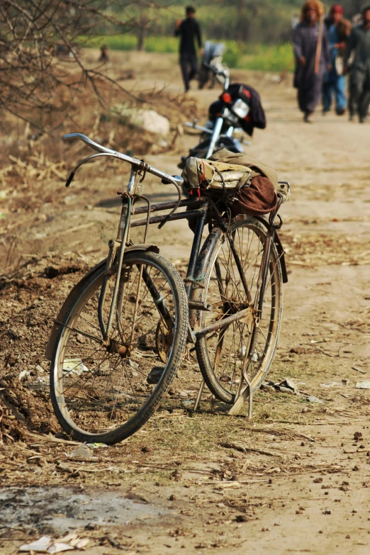 a old bike with a bunch of bags on the back sits by the dirt