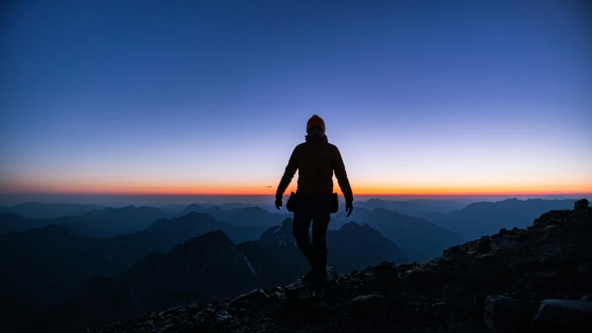 silhouetted hiker walking up a rocky mountain at sunset