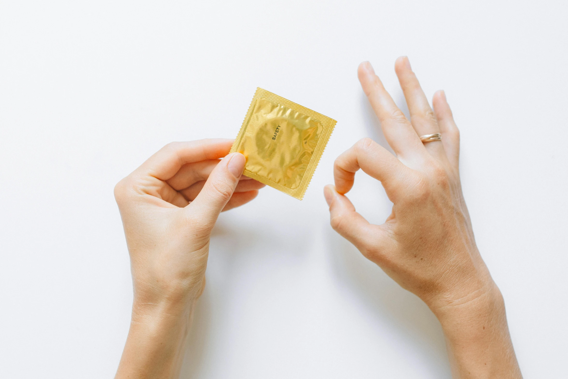 two hands holding a single yellow bag of condom paper